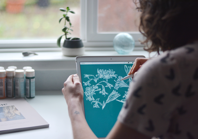 Hiring design help, original artwork and design to brief for your company or product. Image shows Skye McNeill illustrating a botanical pattern on her iPad.