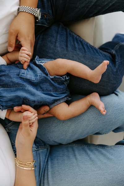 Close-up of baby resting on parents’ laps, all wearing denim, capturing a quiet and tender family moment.