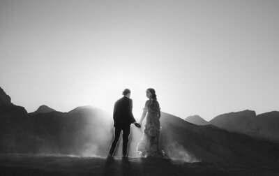 Couple holding hands with backlit sun and hills in grayscale.