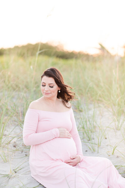 mom holding belly in pink maternity dress at the beach by miami maternity photographer msp photography David and Meivys Suarez