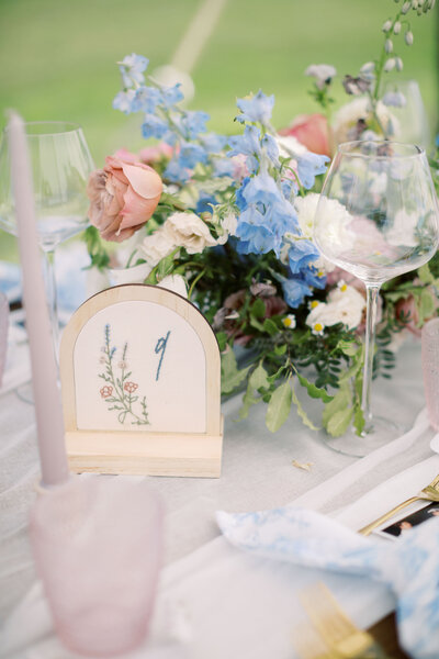 A wedding table with pink and blue flowers, taper flowers, a table number, and a wine glass