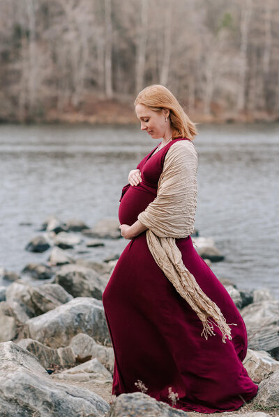 An expecting mother standing at Centennial Lake holding her belly as the wind billows her dress