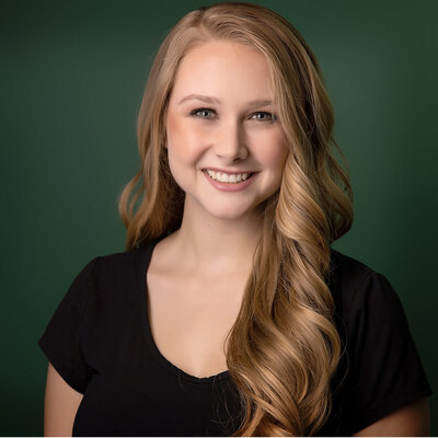 A woman with long wavy blonde hair and a black top smiles in front of a green background, captured beautifully by a Jacksonville headshot photographer.