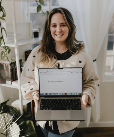 A woman smiling holding a laptop, she has brown hair and is an author.