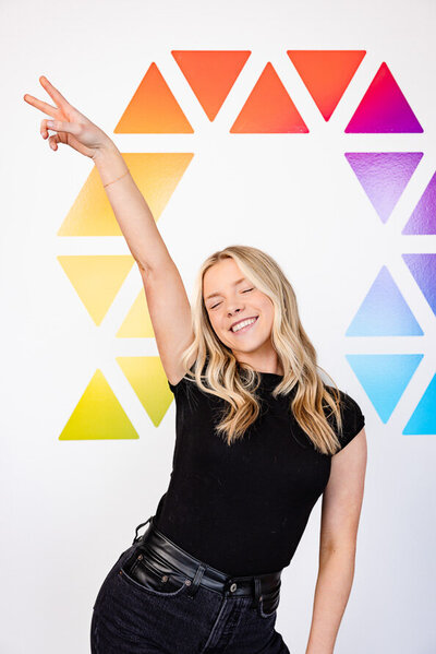 Woman throws peace sign in front of her company's logo for her branding headshots.