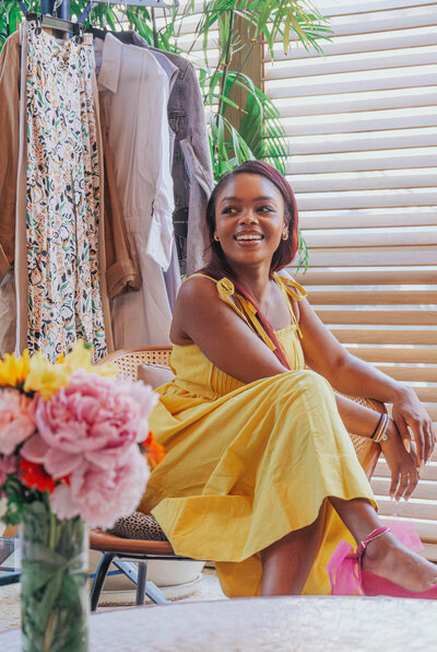 Tahirah in a yellow dress smiling in front of a rack of clothes