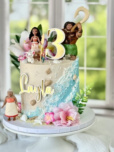 Two-tier purple and gold birthday cake with floral accents and linear art. by Artisan Buttercream
