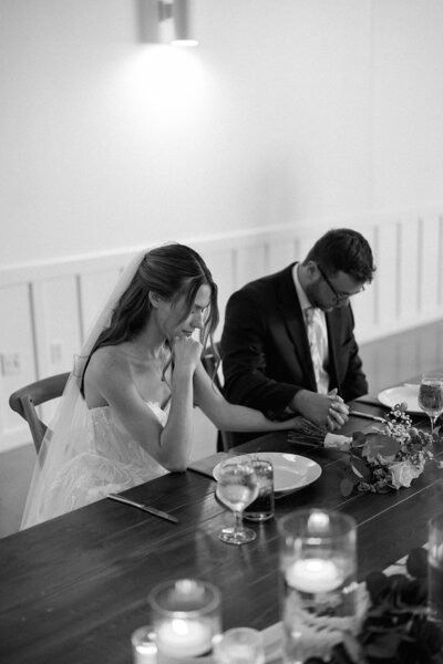 Bride wiping tears during a sentimental wedding reception dinner with her groom, captured candidly in an emotive editorial wedding photography style.