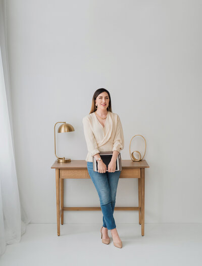 seamless photography studio headshot of kaylyn leighton in front of wood desk.
