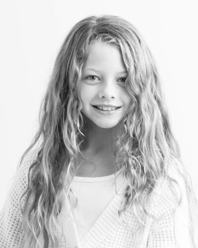 light black and white portrait of little girl with long curly hair against white backdrop