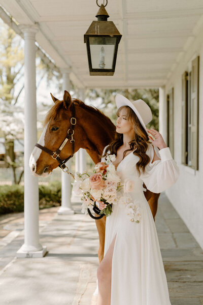 bride wearing a hat standing next to a horse for french inspired wedding