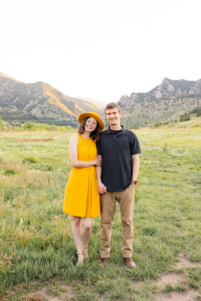 A wife holds onto her husband's forearm and they both smile at the camera.