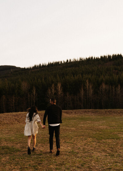 Couple running through a field in view of Montana Mountains