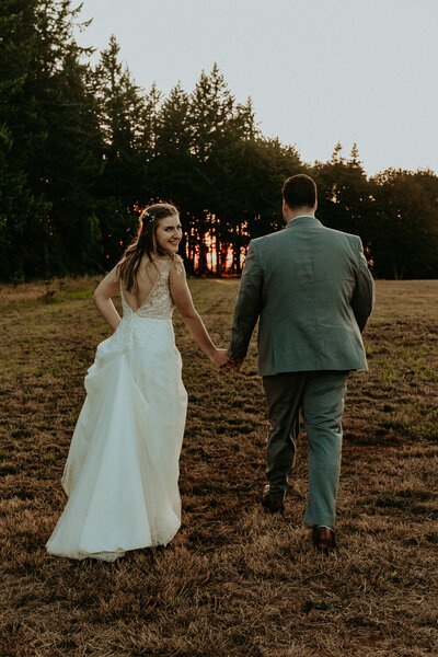 Married couple walking away while holding each other's hand and bride looking bac