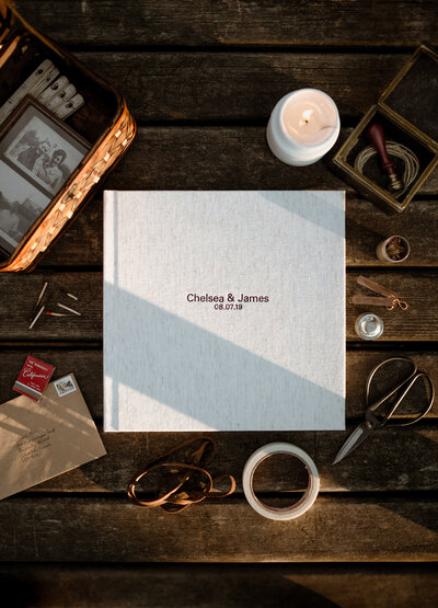 A flatlay photo of a wedding album front cover made of linen with antique tools around it