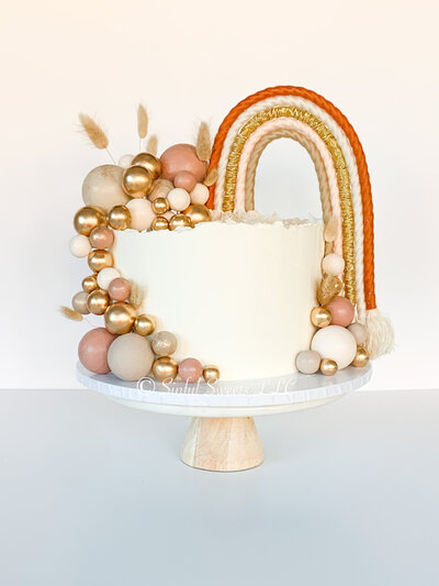 Full image of a white cake with a rainbow and gold decorations on either side. Cake sits on a marble cake stand.