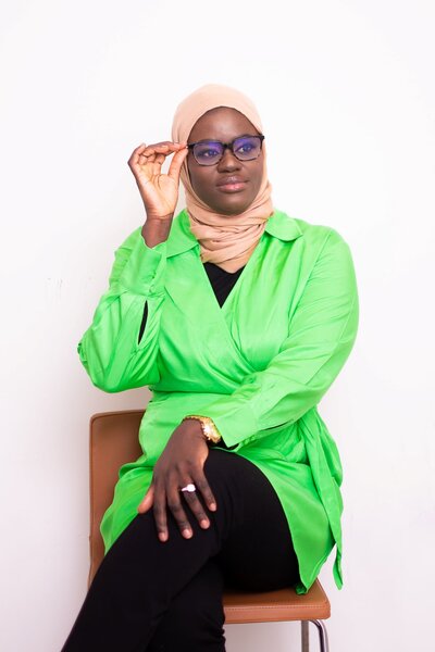 Photo of Isatou Bittaye Jobe, a grant writing consultant, wearing a lime green tunic and smiling confidently. The background a is professional white space and she is sitting in a brown chair