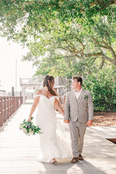 A happy married couple holding hands and walking the Wilmington oceanside boardwalk on their wedding day while enjoying their destination wedding photos