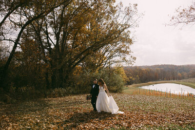 Bride and groom holding hands walking through fall leaves in a golden glow