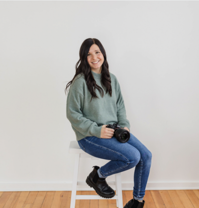 Photographer holding her camera, smiling on a stool.