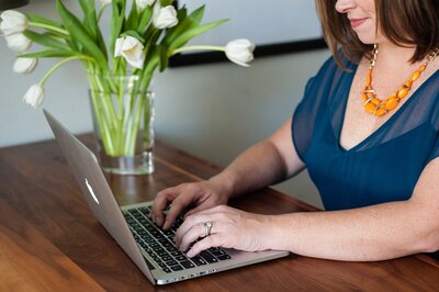 woman in a blue blouse typing on a laptop computer at a desk 