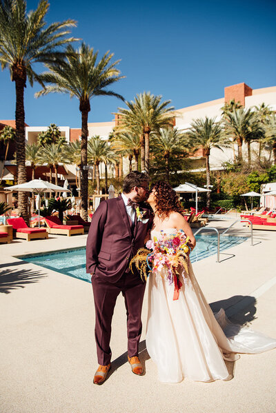 A bride and groom kissing while standing on a pool deck.