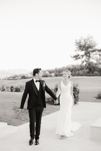 black and white image of bride and groom walking holding hands
