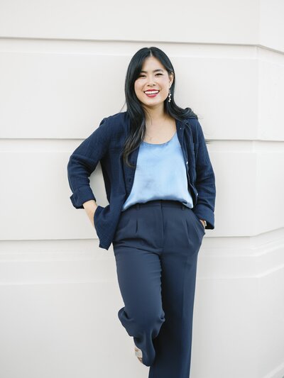 A woman leaning on a white building in NYC smiling at the camera during her brand session