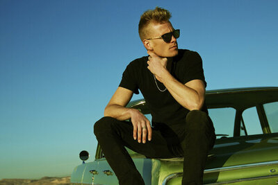 Musician photo Ryan Guldemon sitting on trunk of green classic car wearing sunglasses and looking over his shoulder