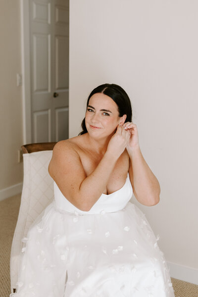 bride poses for camera in wedding dress while fixing her hair.