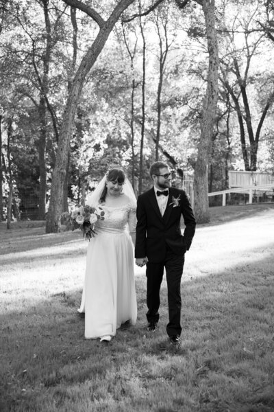 Austin-based wedding photographer captures a stunning black and white photo of a bride and groom walking in the woods.