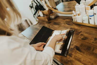 balayage specialist and hair extension professional flipping through custom color extension options 