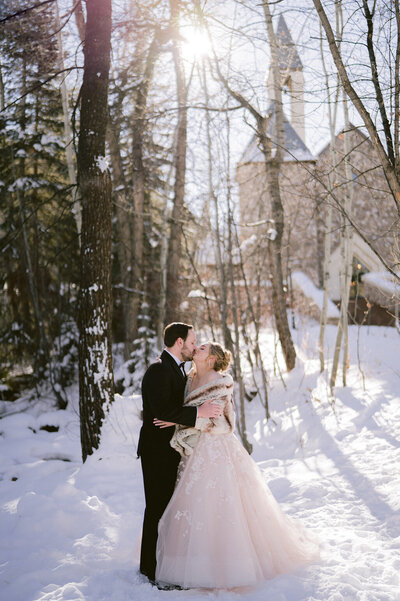 Bride and groom, clients of E Stokes Creations sharing a romantic kiss outside Beaver Creek Chapel on their wedding day