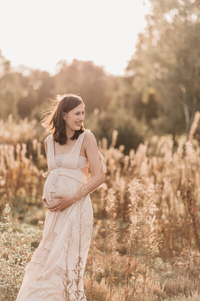 Photo of a pregnant woman standing in the sunset wearing a cream maxi dress