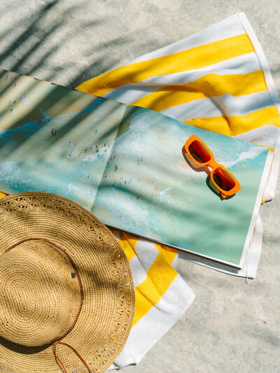 Book, straw hat, and orange sunglasses laying on a yellow striped towel