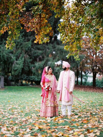 indian bride and groom in traditional outfits posing in a park holding hands