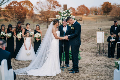 woman in white dress holding hands with man in black tux standing in front of a cross outside