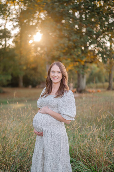 Beautiful mother embracing her pregnant belly while the sun sets behind her