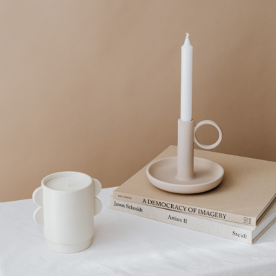 A neutral colored image picturing two candles and two books on a table with a white tablecloth