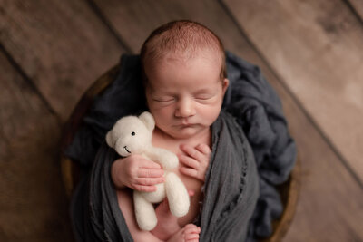 Studio photograph of a newborn baby boy holding a stuffed bear
