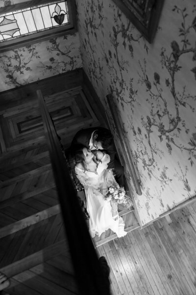 Bride and groom sharing a kiss on a grand staircase during their wedding, captured from above for a romantic and artistic perspective.