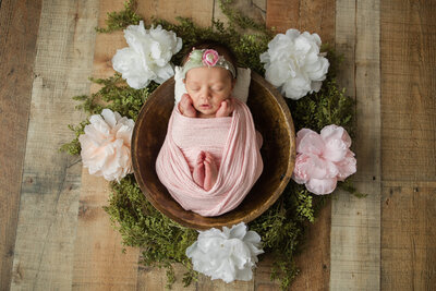 Newborn baby girl wrapped up in a bowl surrounded by flowers