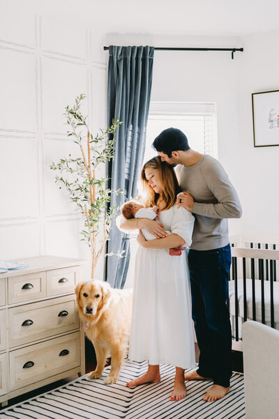 couple holding baby in nursery with dog