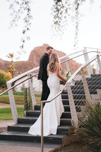 Bride and groom walking upstairs at Mountain Shadows resort wedding in Scottsdale with desert cactus and Camelback Mountain in the background.