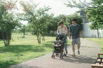 柔らかな光の中パパとママと赤ちゃんがベビーカーで公園をお散歩しているシーン