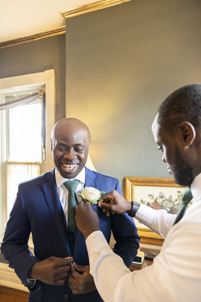 A person helping someone pin a boutonniere on their wedding day 