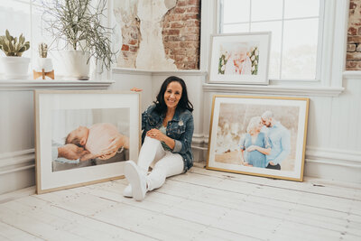 A photographer sitting and smiling while surrounded b y framed family photos