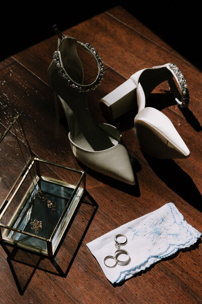 Brides wedding shoes are nude heels with rhinestones and pearls next to her ring box.