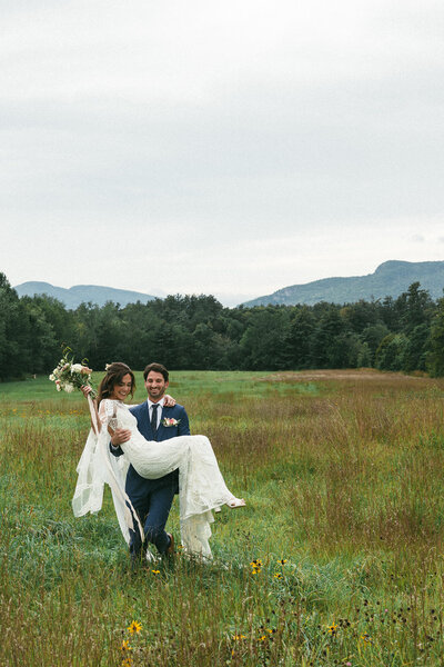 Groom carrying his bride through a field in the mountains bohemian wedding photography