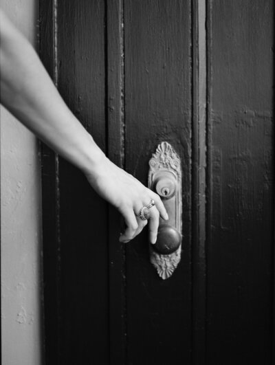 woman's hand with ornate gold and stone jewelry reaches for ornate door knob and plate, film brand jewelry photography